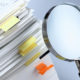 magnifying glass looking at a stack of reports